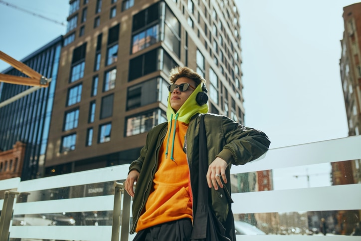 Young cool attitude man, student posing against urban, city views. model dressed trendy, neon oversized clothes. Concept of street fashion and urban style, modern lifestyle, gen Z, self-expression.